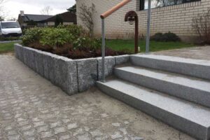 Trappen er lavet i granitblokke, hvorfra en sti af betonfliser fører hen til husets indgangsparti. Kanten af bedet er lavet af granit kantsten sat på højkant, hvilket giver en højere kant på ca. 45 cm